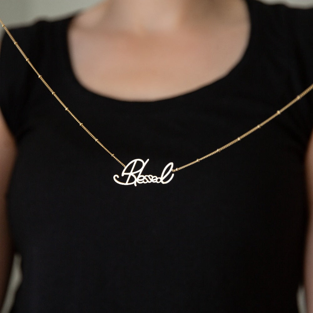 blessed necklace suspended in front of a woman wearing a black shirt