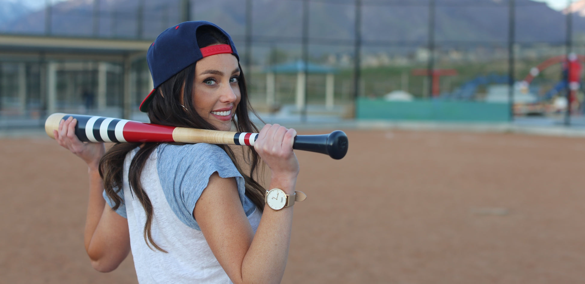 woman with a softball bat on a softball field wearing a Arvo Awristacrat gold watches for women with white dial, gold case, and nude or tan leather band