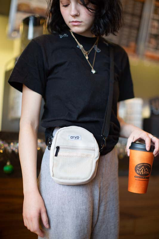 young woman wearing an Arvo crossbody bag that is a light tan color called wheat