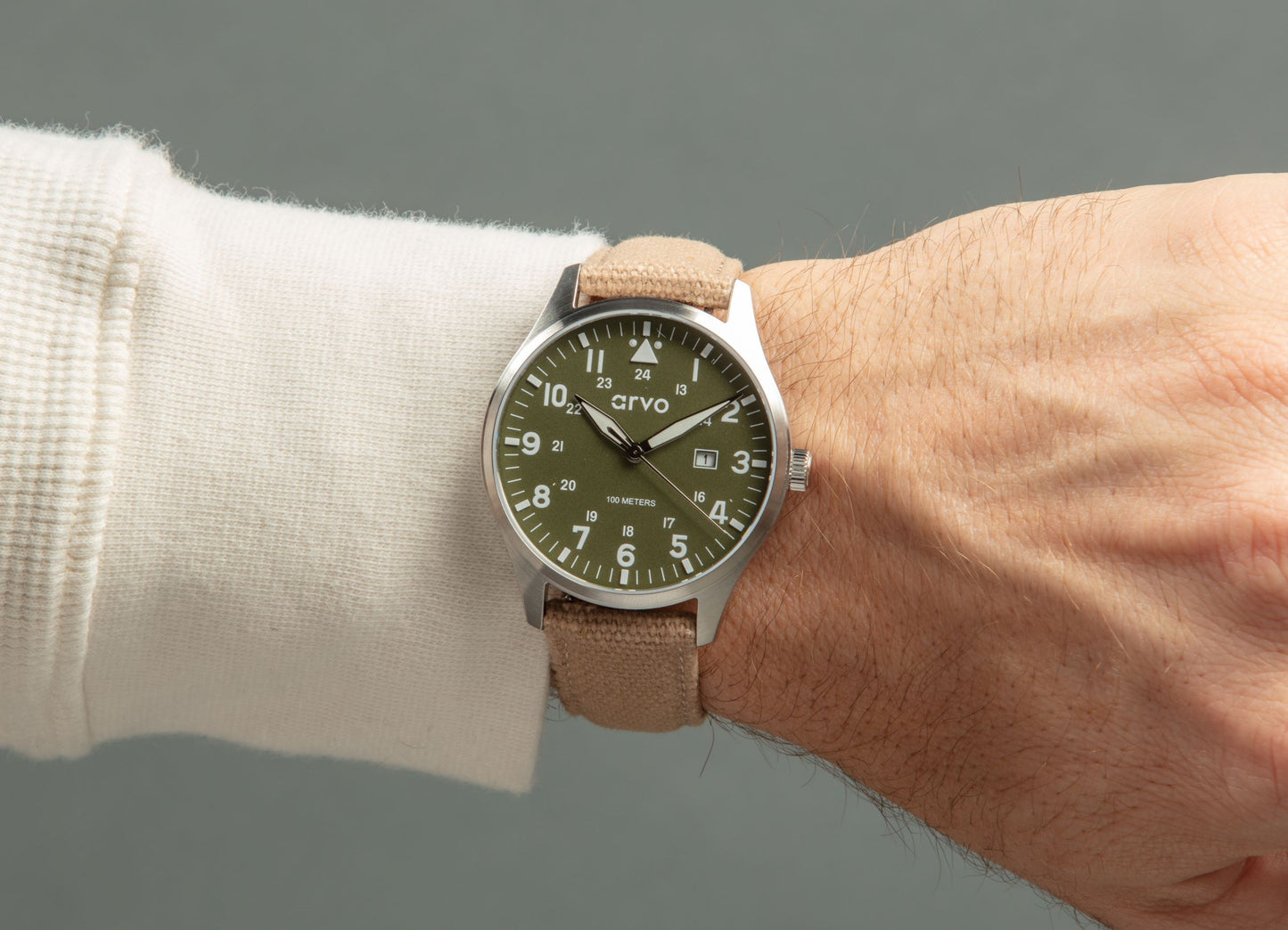 Man's wrist wearing an Arvo Rove Field Watch for men with a spring green dial and khaki canvas strap