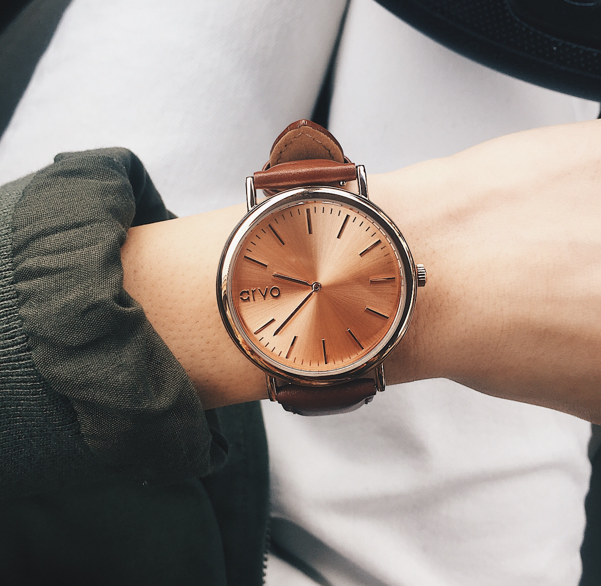Arvo Rose Time Sawyer Watch for men and women with rose gold dial and rose gold case with a brown stitched leather band on a wrist beside a green blouse sleeve