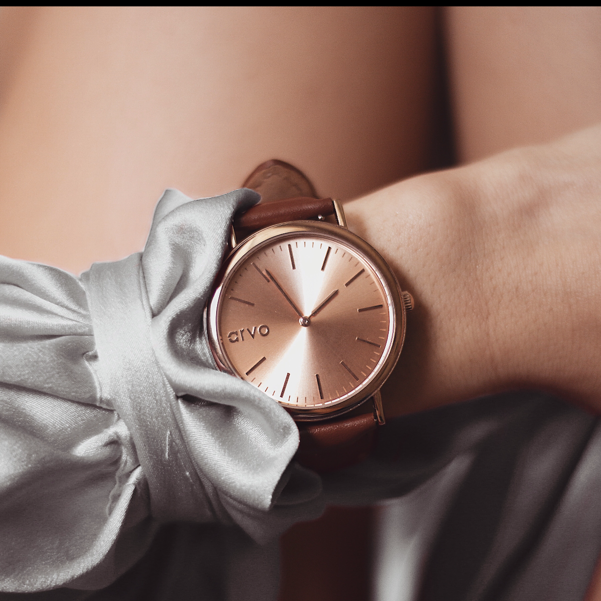 Arvo Rose Time Sawyer Watch for men and women with rose gold dial and rose gold case with a brown stitched leather band on a wrist nestled beside a light gray blouse sleeve