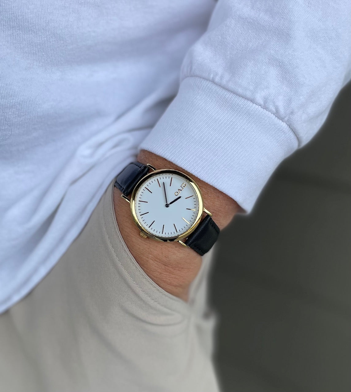 Arvo Time Sawyer Watch for men and women on a man's wrist. His hand is in his pocket. Watch features a white dial, gold case, and black leather band
