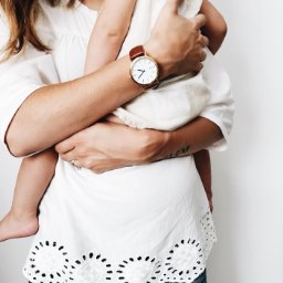 woman holding a toddler wearing a Time Sawyer watch for men and women white dial, gold case, and brown leather band