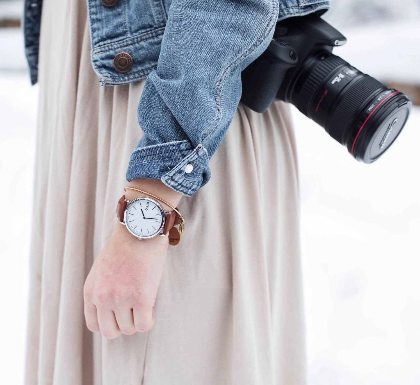Woman carrying a camera wearing a Time Sawyer Watch for men and women with white dial, silver case and brown leather band